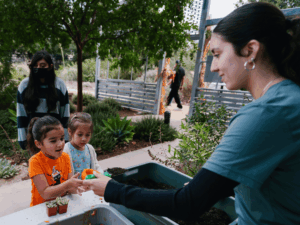 Waterwise Community Center volunteer helps a child fill her pumpkin with dirt for a pumpkin succulent centerpiece.