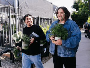 Two community members walk happily with plants in their arms that they bought from the Waterwise Community Nursery.